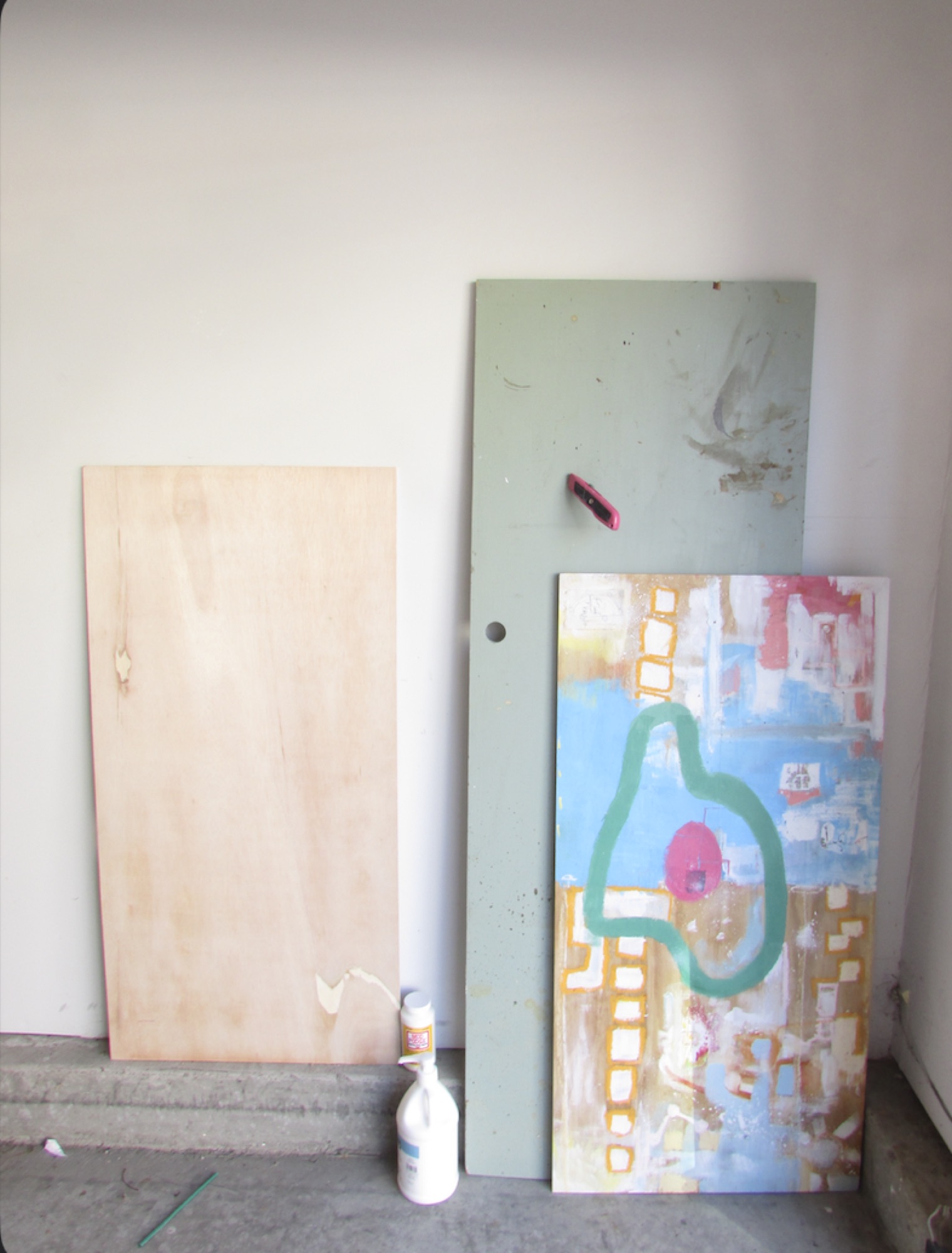 A painted panel leaning against a wall beside a door.